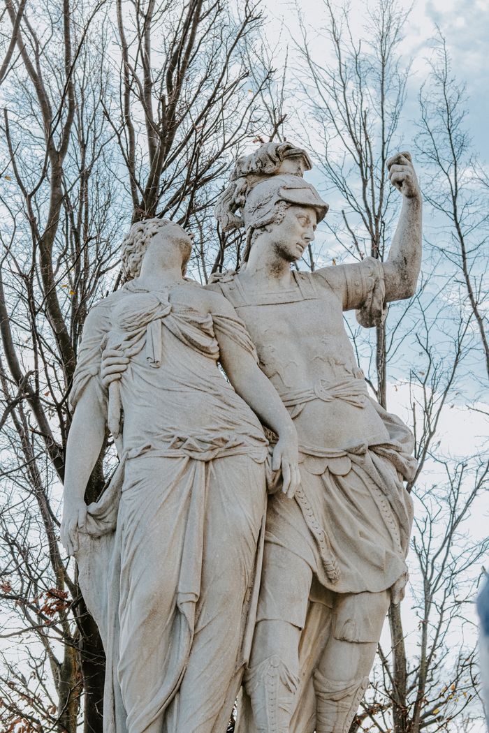 Elegant marble statues of figures in a park with a clear spring sky overhead.
