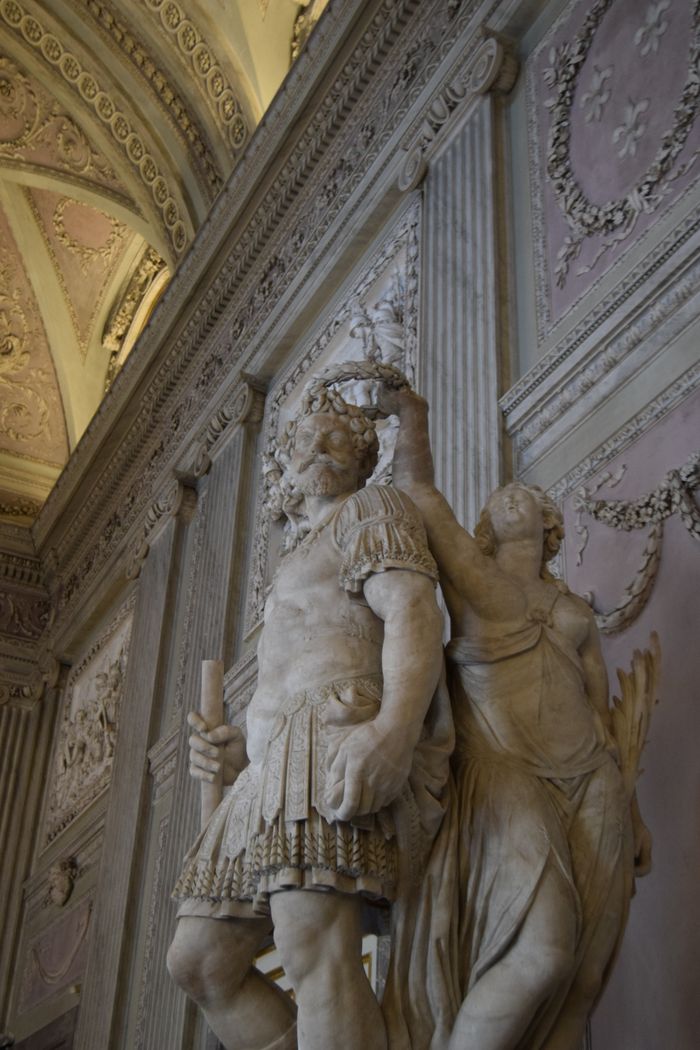 Close-up of classical marble sculptures inside an ornate museum hall with detailed frescoes.